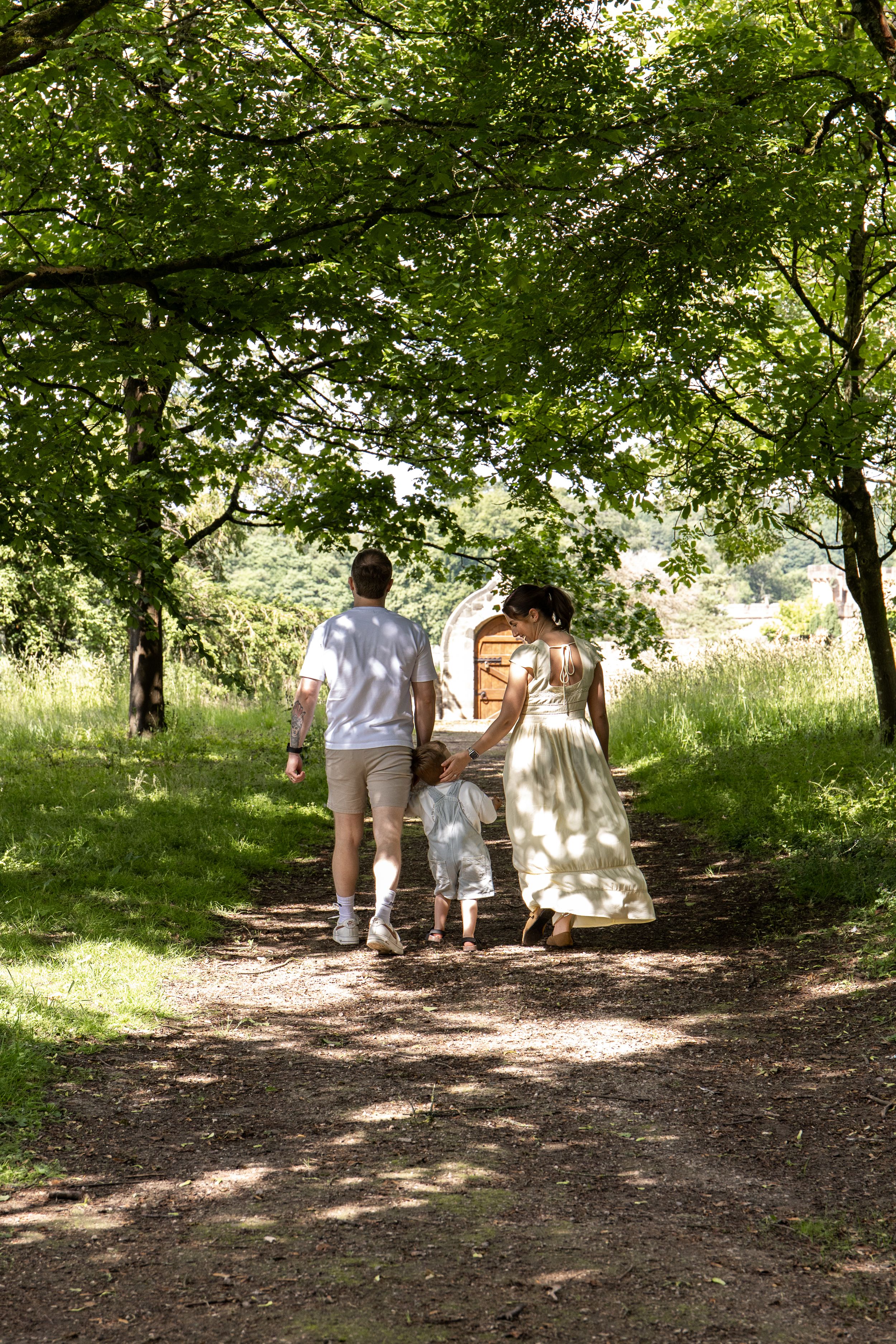 Family walking hand-in-hand along a sunny tree-lined path on a bright summer day natural Outdoor family photoshoot Nottingham