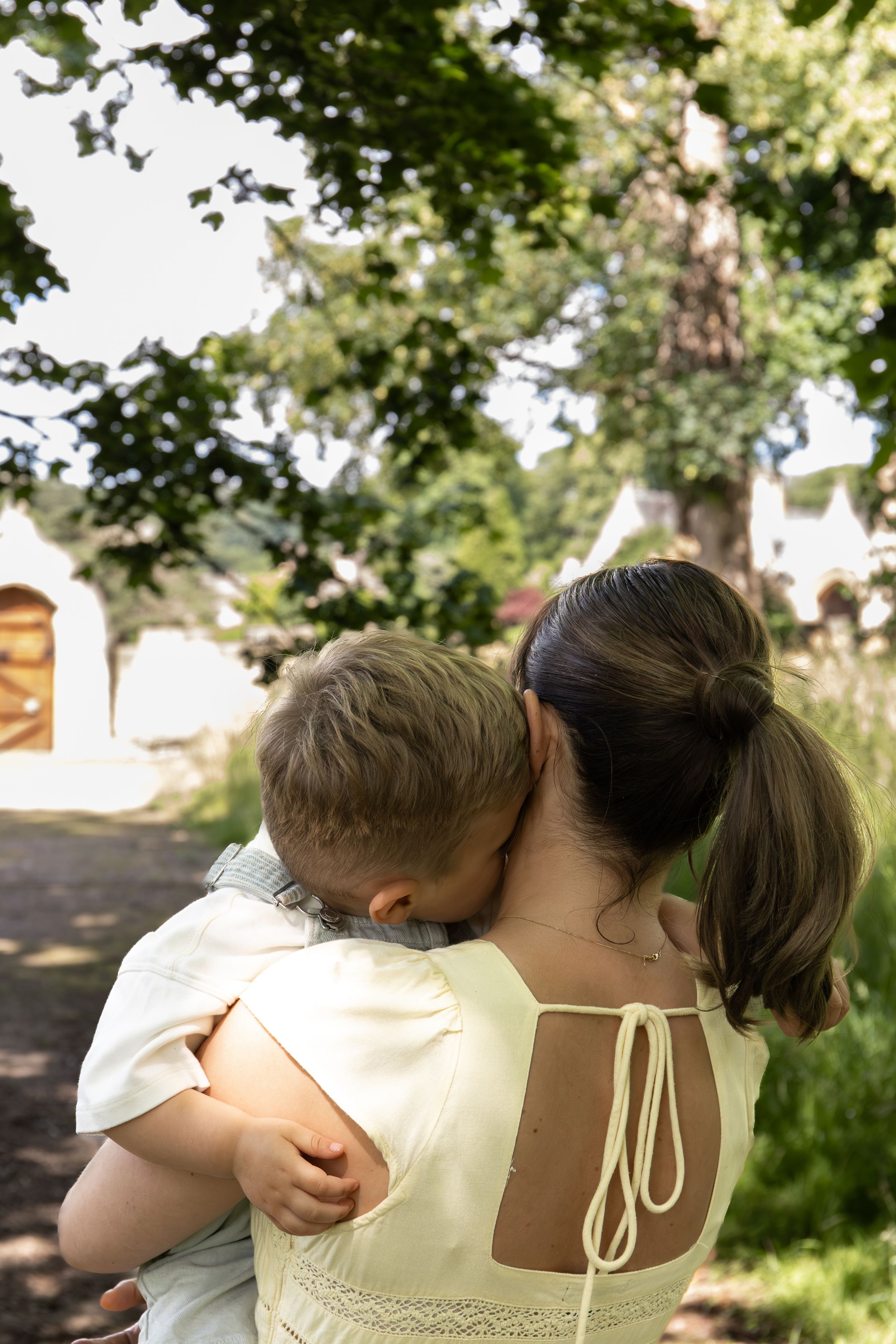 A mother holds her young child in her arms outdoors, surrounded by lush green trees natural Outdoor family photoshoot Nottingham