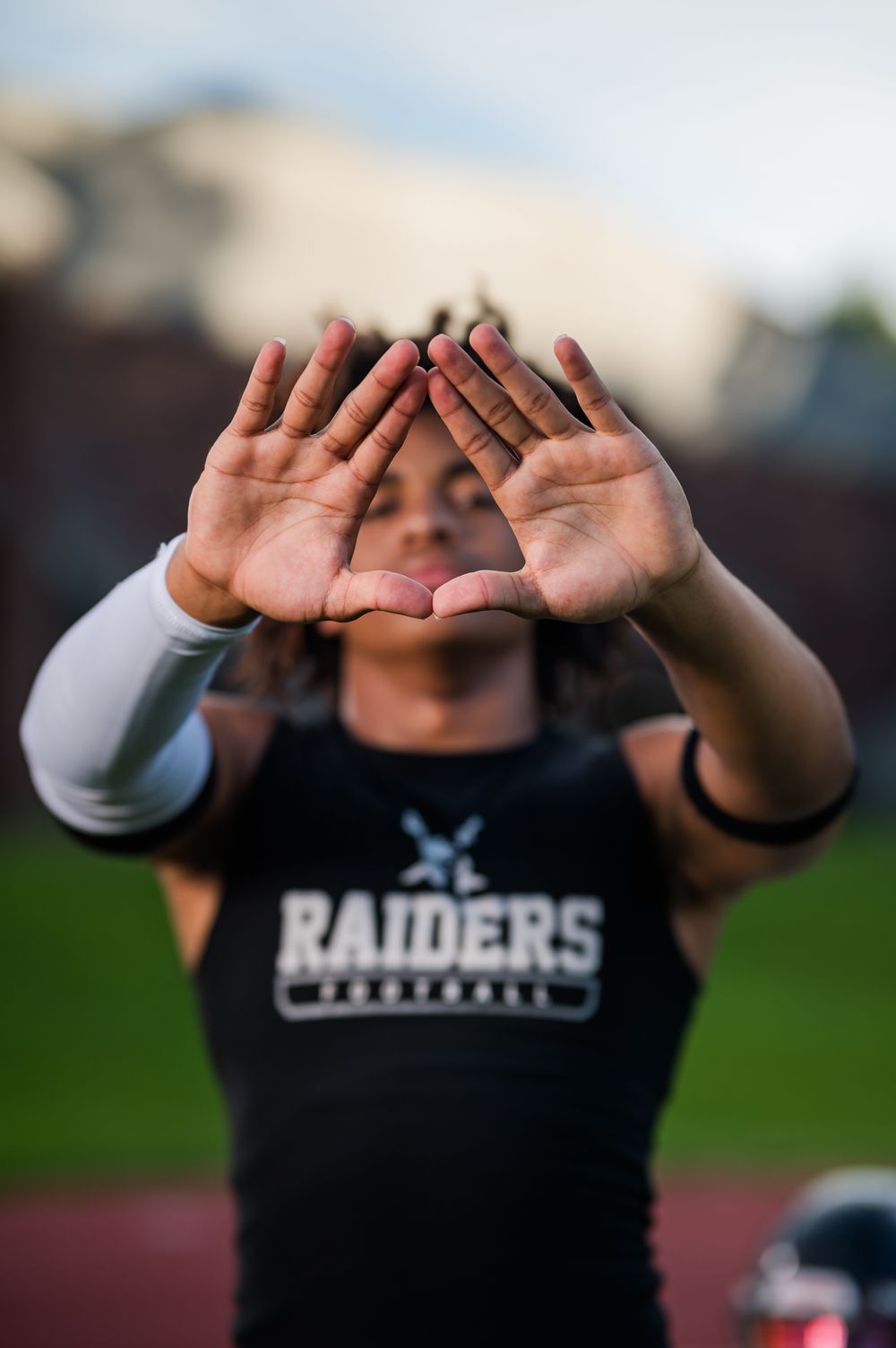 Raiders football player holds hands up forming a diamond shape, wearing black jersey and white arm sleeve.