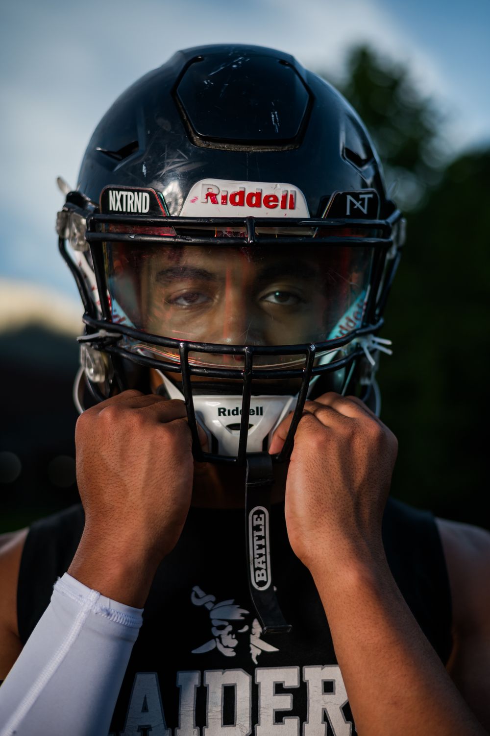 A Raiders football player adjusts his Riddell helmet chin strap before a game.