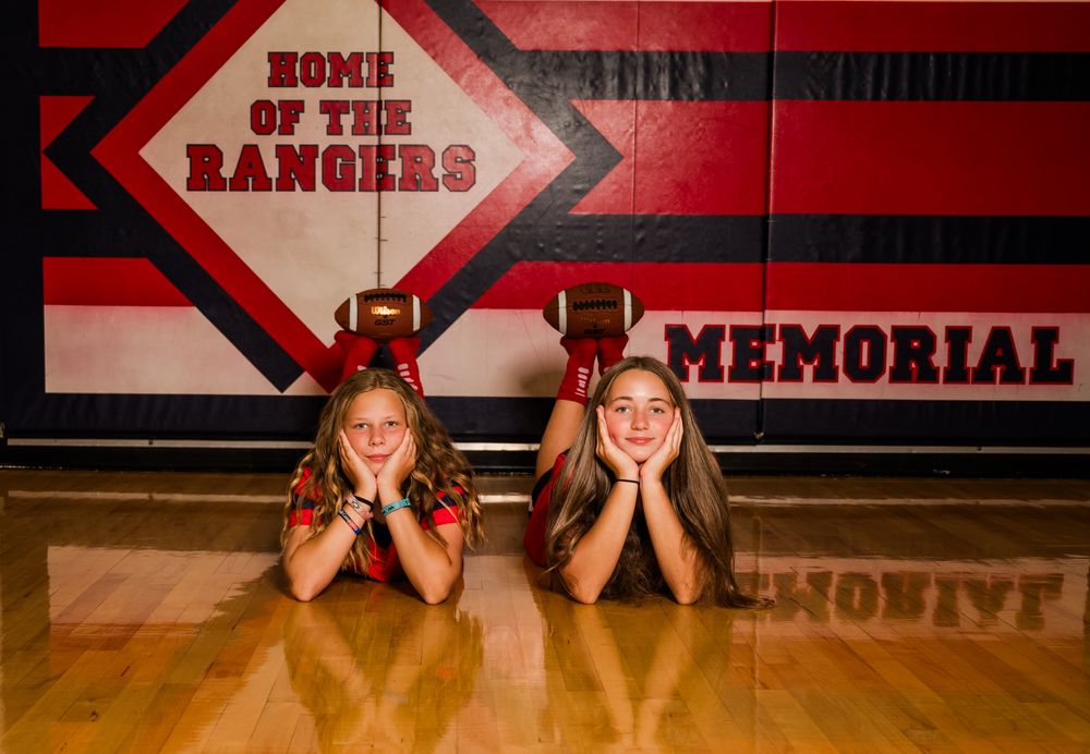 Two girls lying on a gym floor in front of a Home of the Rangers Memorial school gymnasium wall mural.