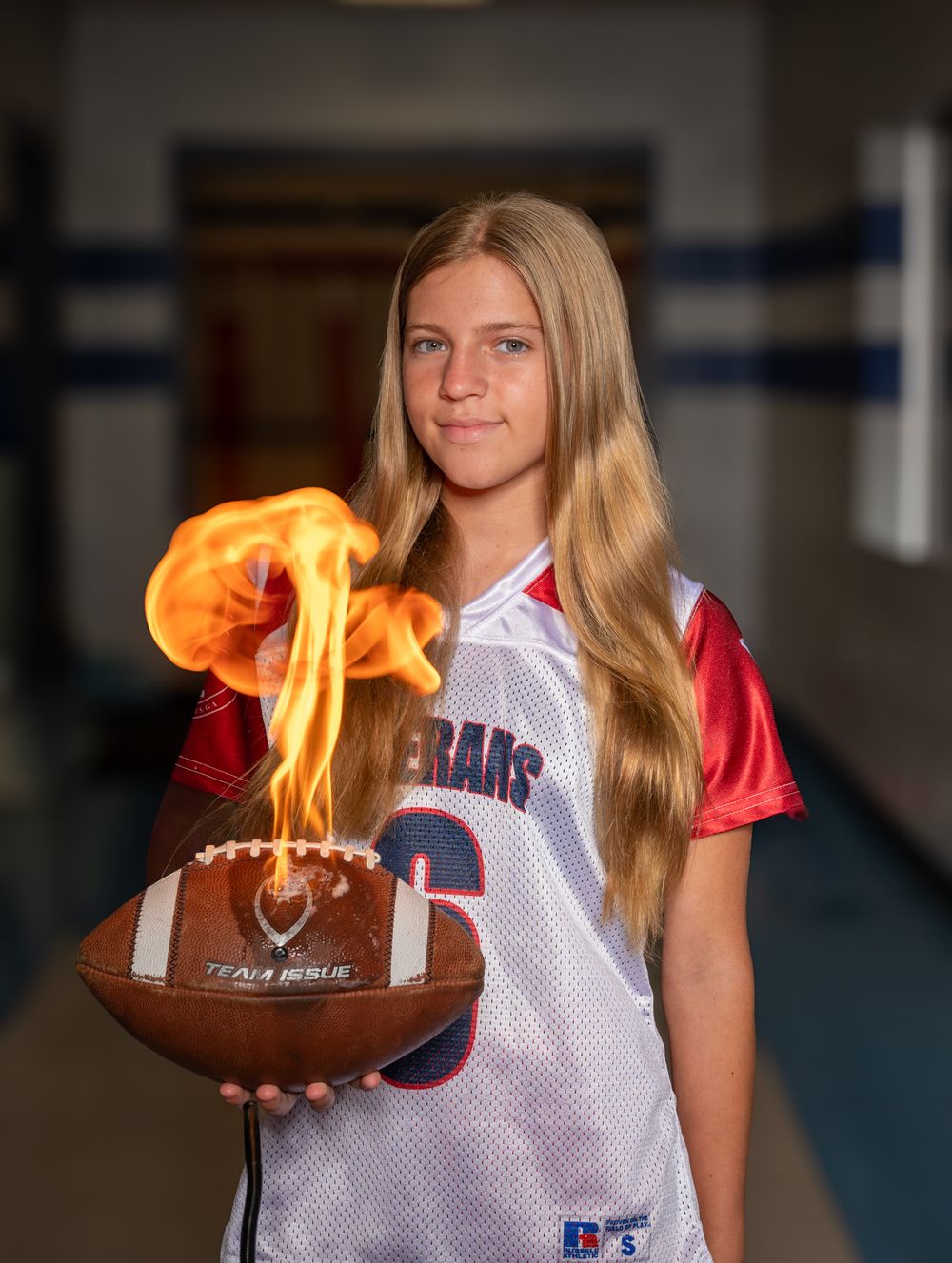 Young female athlete in Veterans jersey holds a flaming football in a school hallway.