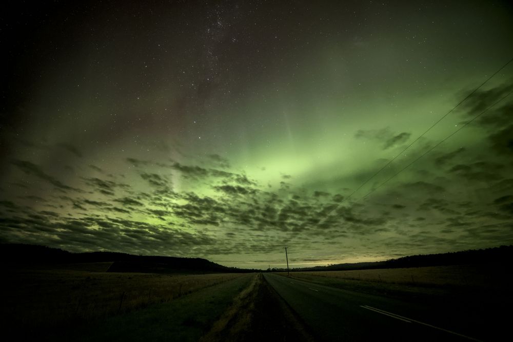Stunning green aurora australis over straight rural road with fisheye perspective and dramatic cloud formations.