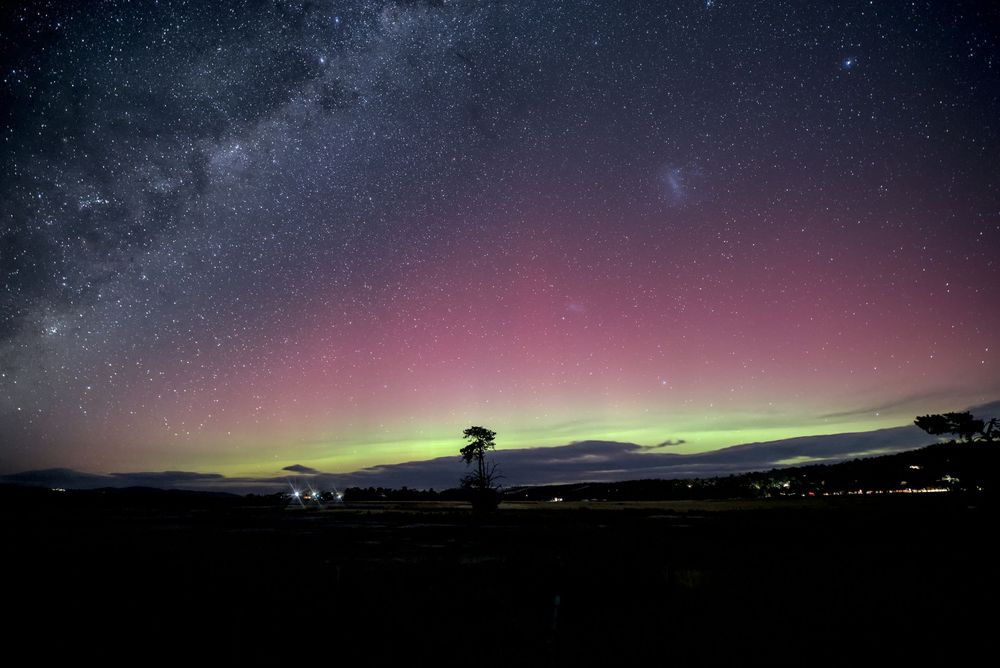 Aurora australis illuminates night sky with vibrant pink and green lights over dark silhouetted landscape and starry sky.