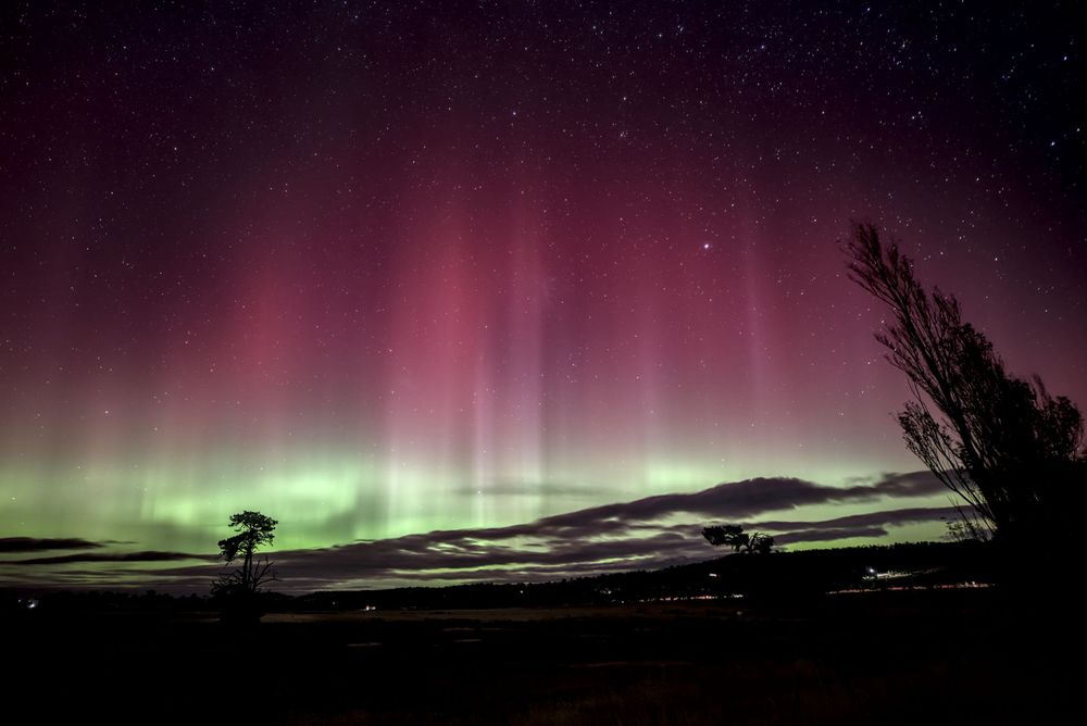 Stunning aurora australis display with vibrant green and red lights illuminating the night sky over a dark landscape.
