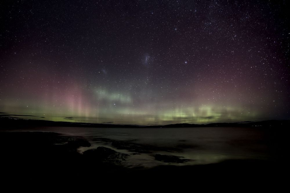 Aurora borealis northern lights dancing over a calm lake reflecting green and purple hues under a starry night sky.