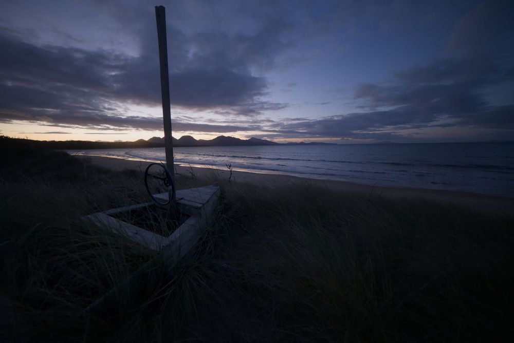 Twilight seascape with concrete post in foreground, mountains silhouetted on horizon.