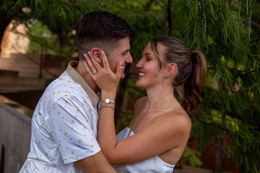 Romantic couple sharing an intimate moment outdoors, smiling face to face under lush green tree branches.