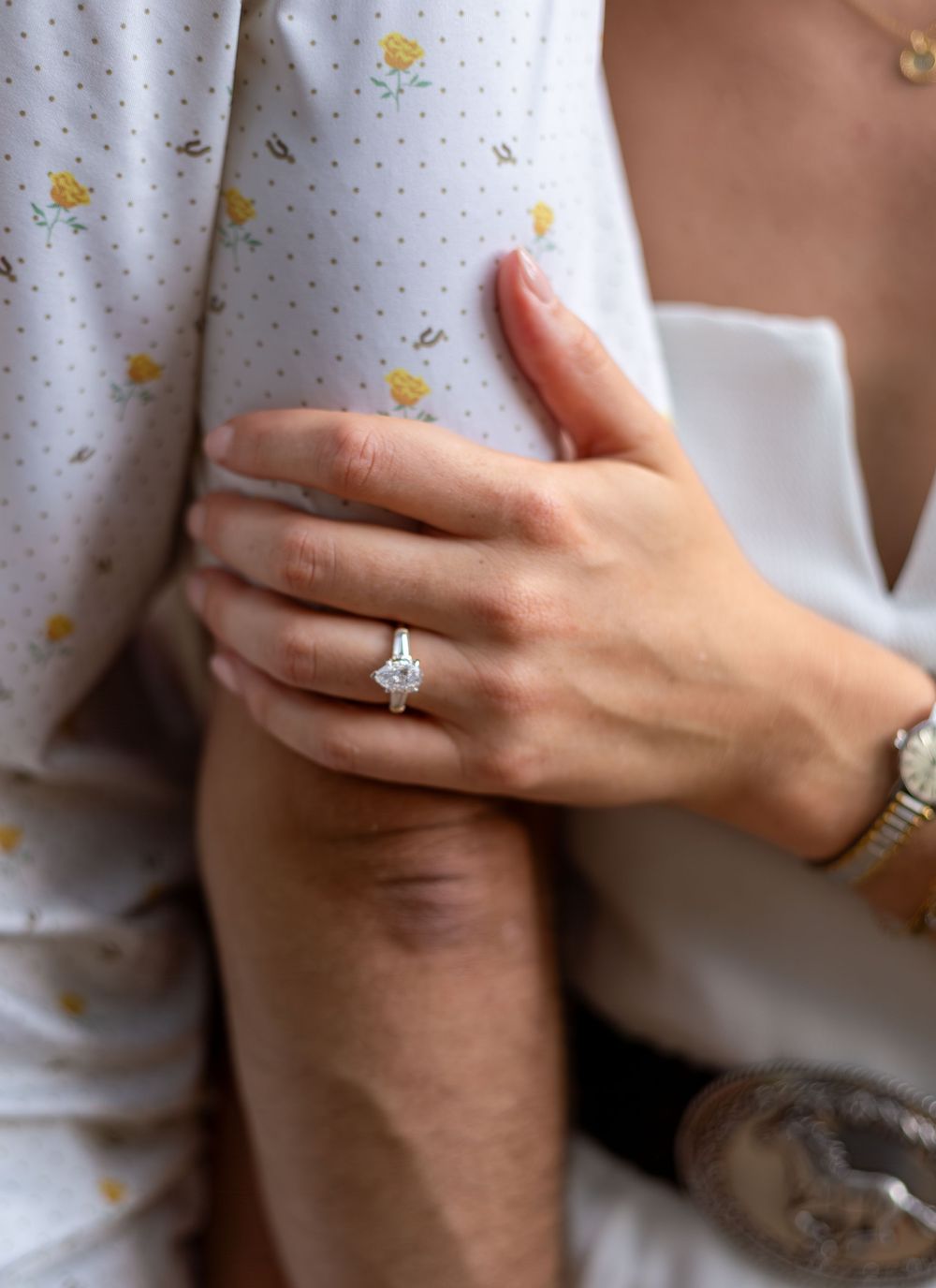 Close-up of a woman's hand wearing a stunning princess-cut diamond engagement ring while embracing a man.