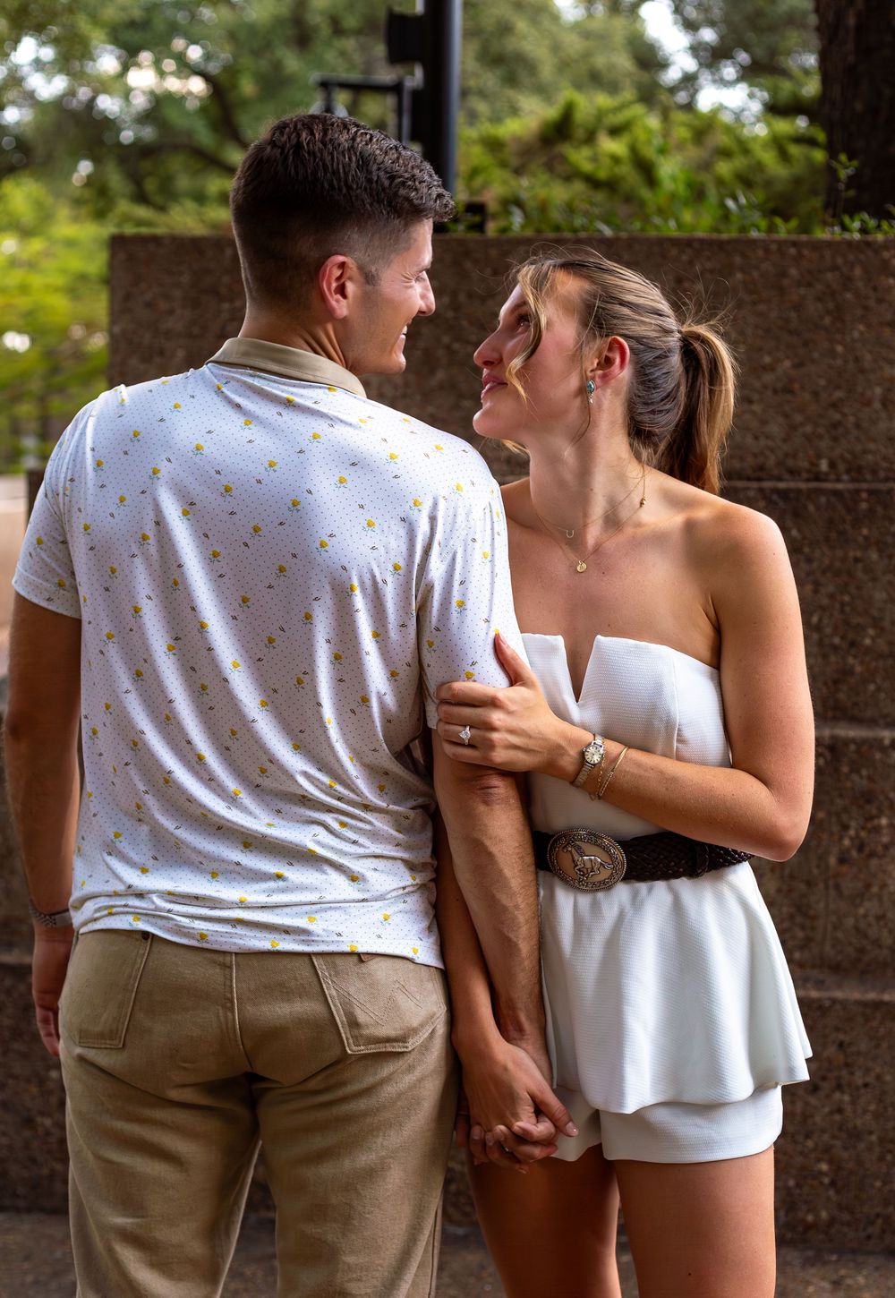 Happy couple sharing a romantic moment outdoors, woman wearing a white outfit with a diamond engagement ring.