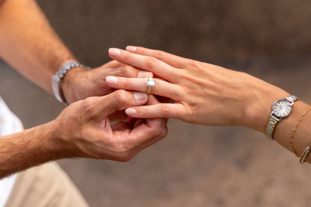 Close-up of a man placing an engagement ring on a woman's finger.