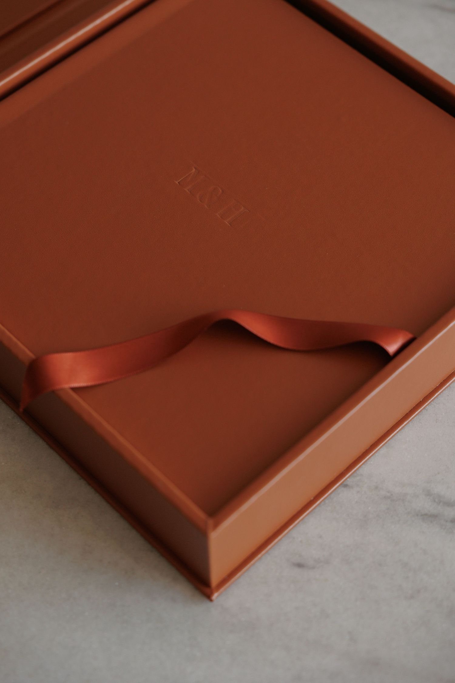 Elegant terracotta gift box with satin ribbon and embossed monogram on marble surface.