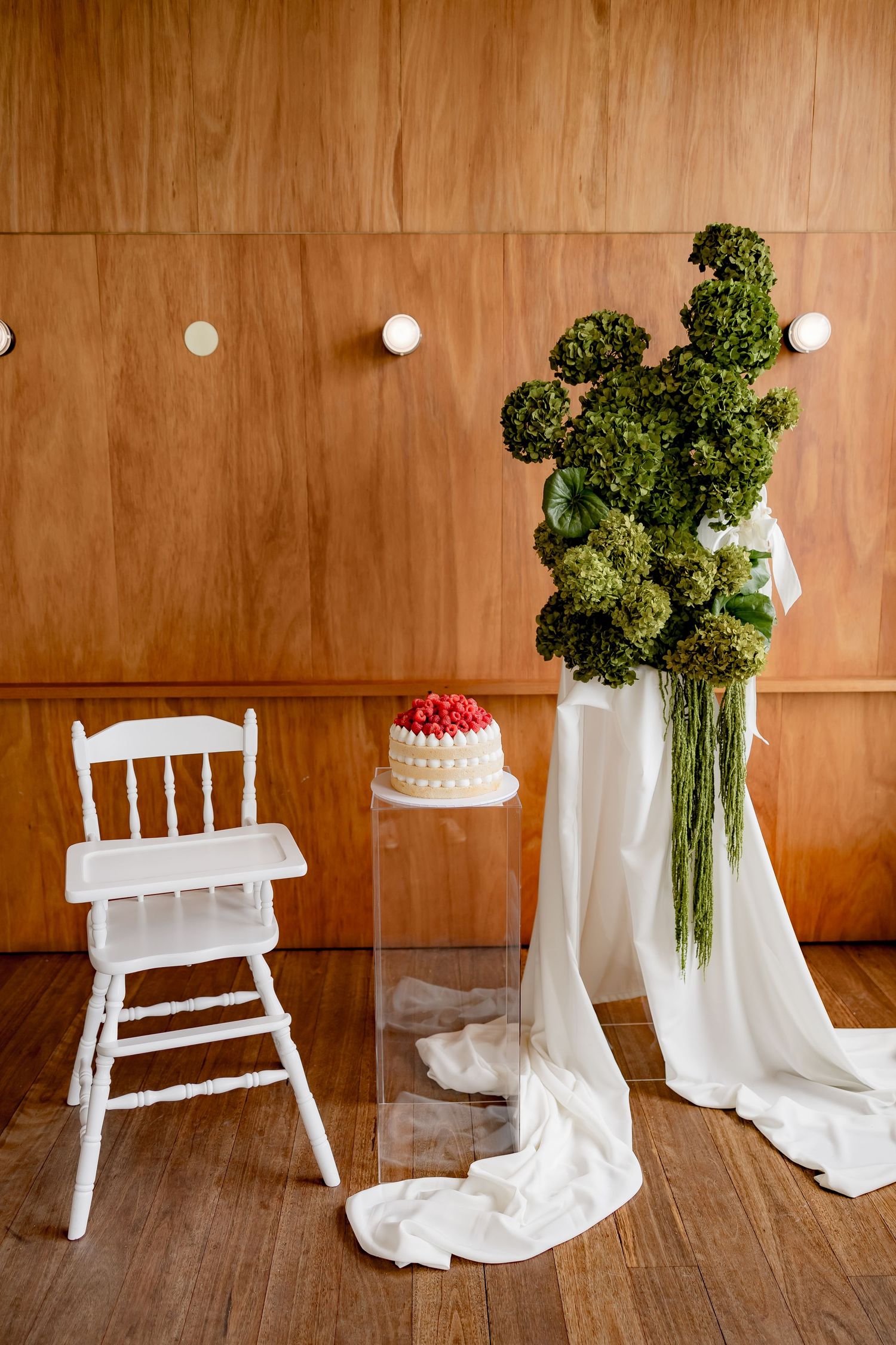 A wedding cake being decorated with delicate white frosting details against a textured stone wall background.