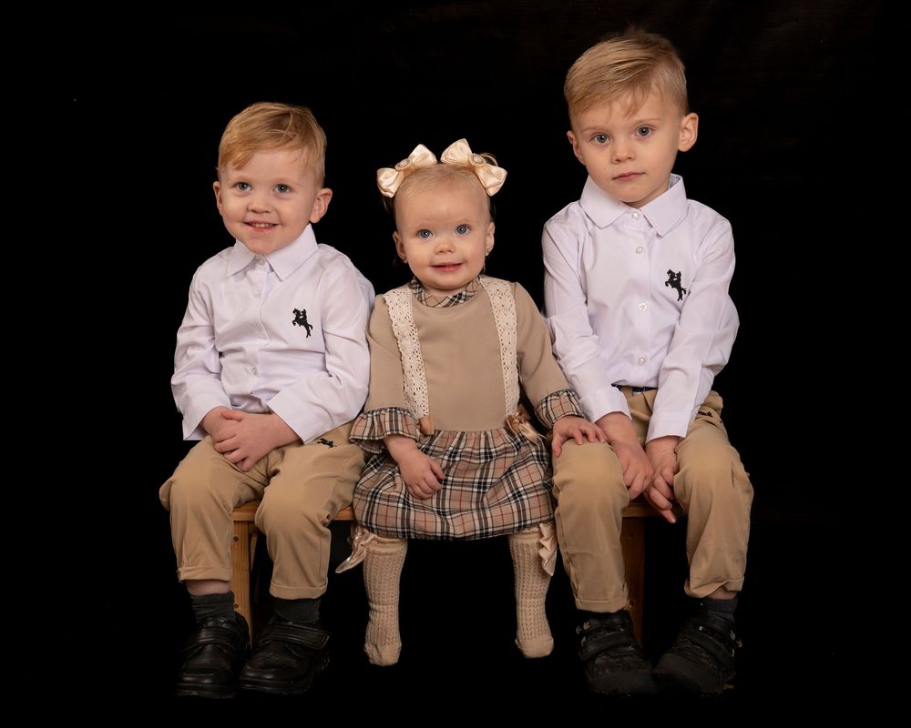 Children sitting together in coordinated outfits against a black background in a professional portrait series.