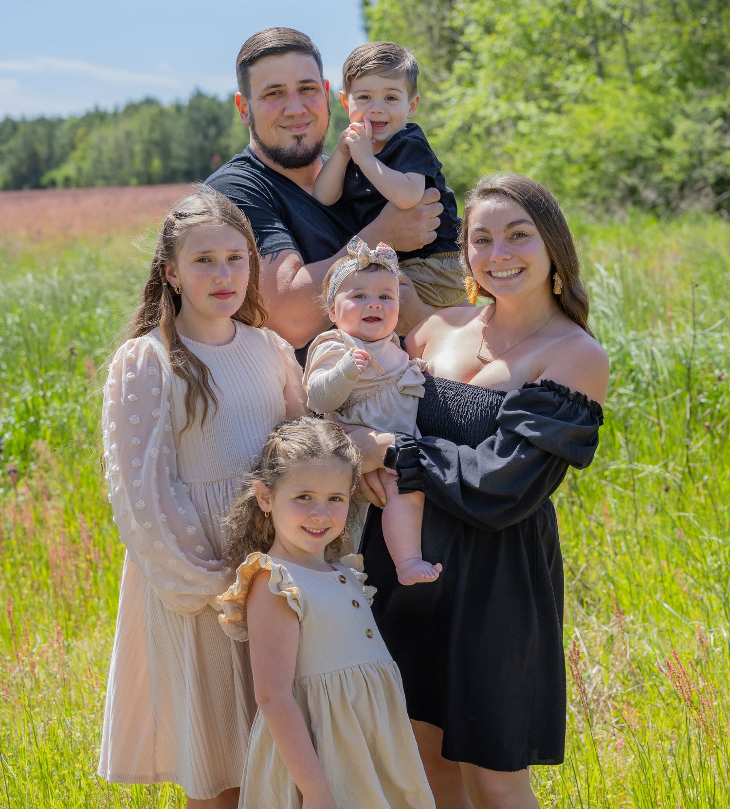Family group portraits in coordinated outfits against lush green summer landscape.