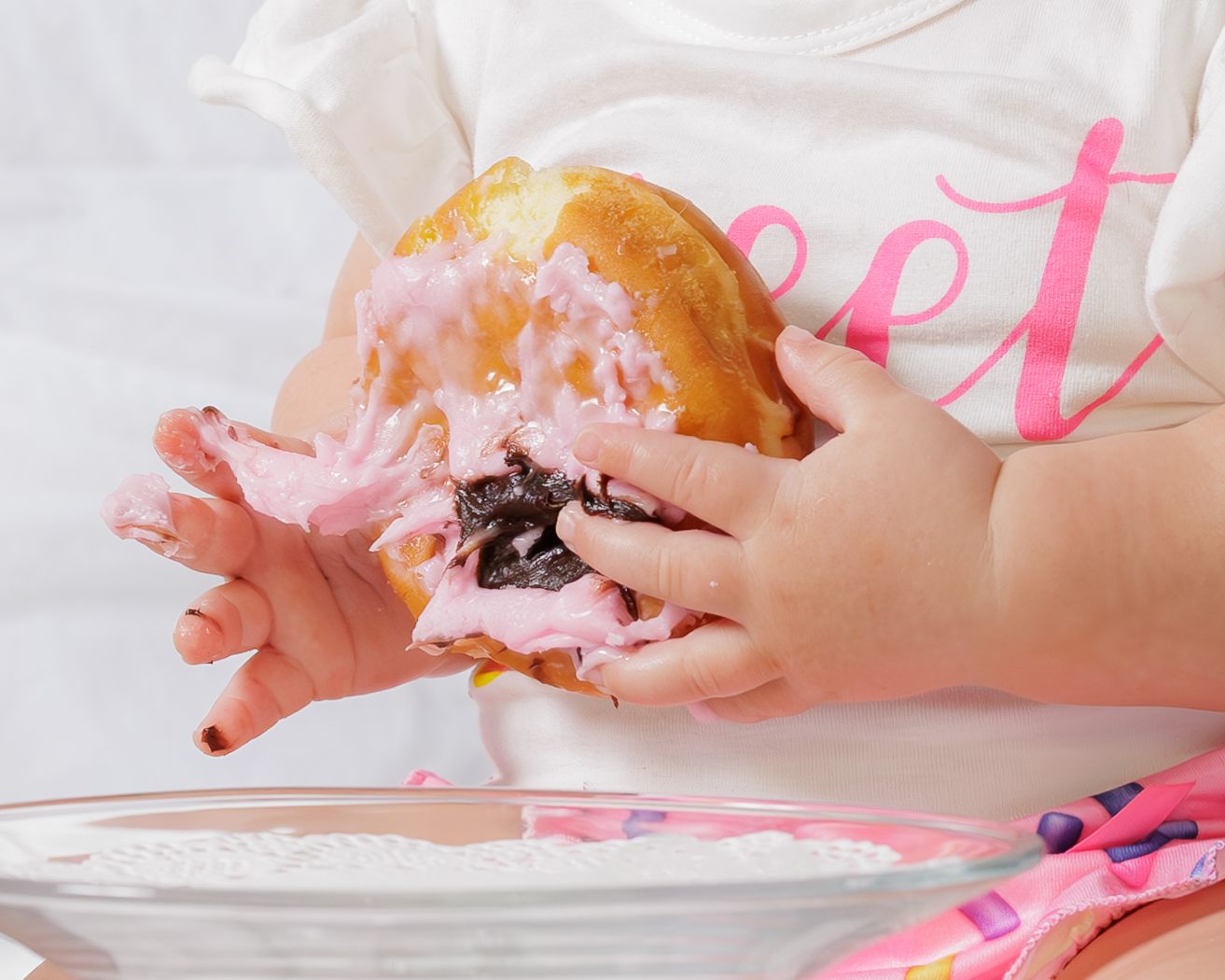 Small hands reaching for and breaking apart a pink frosted donut.