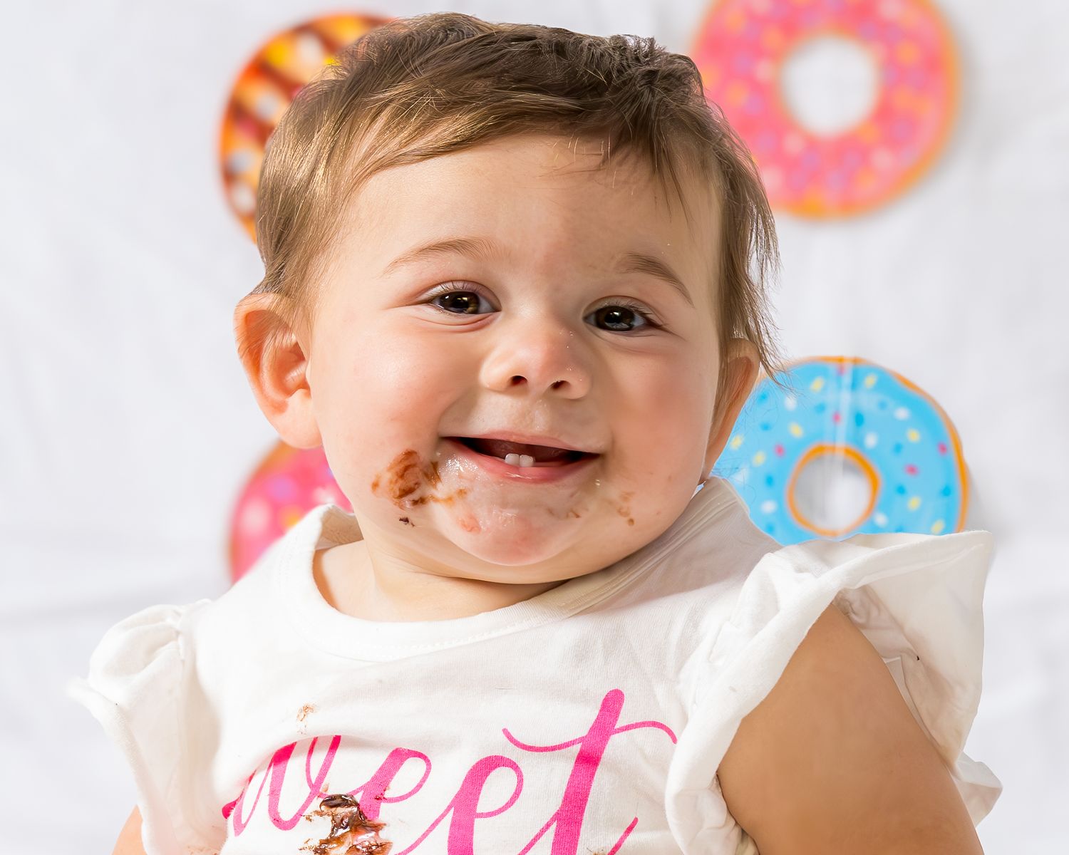 Smiling baby with chocolate smeared face during first birthday donut smash photoshoot.