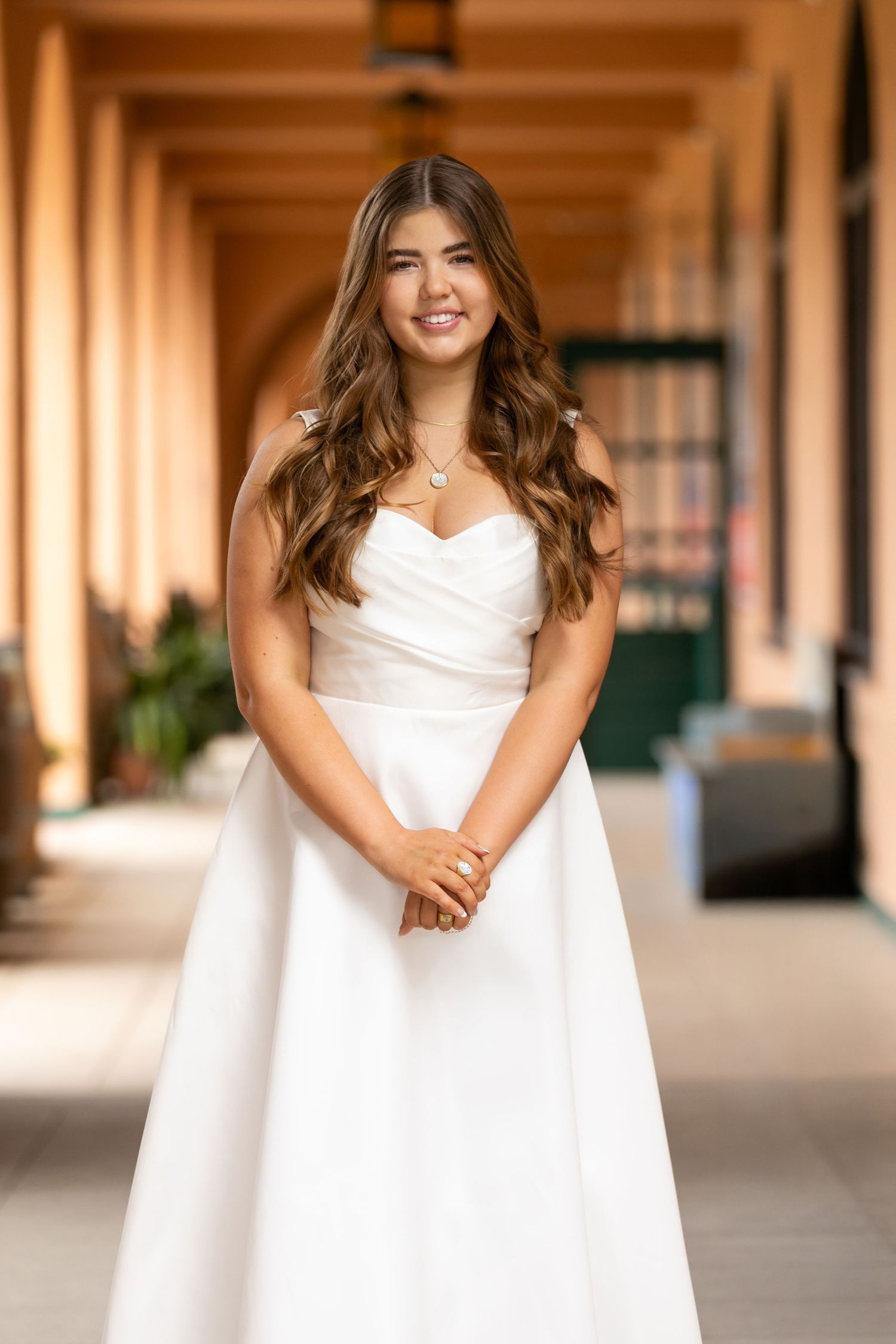 A woman in a flowing white wedding dress stands in an elegant archway corridor.