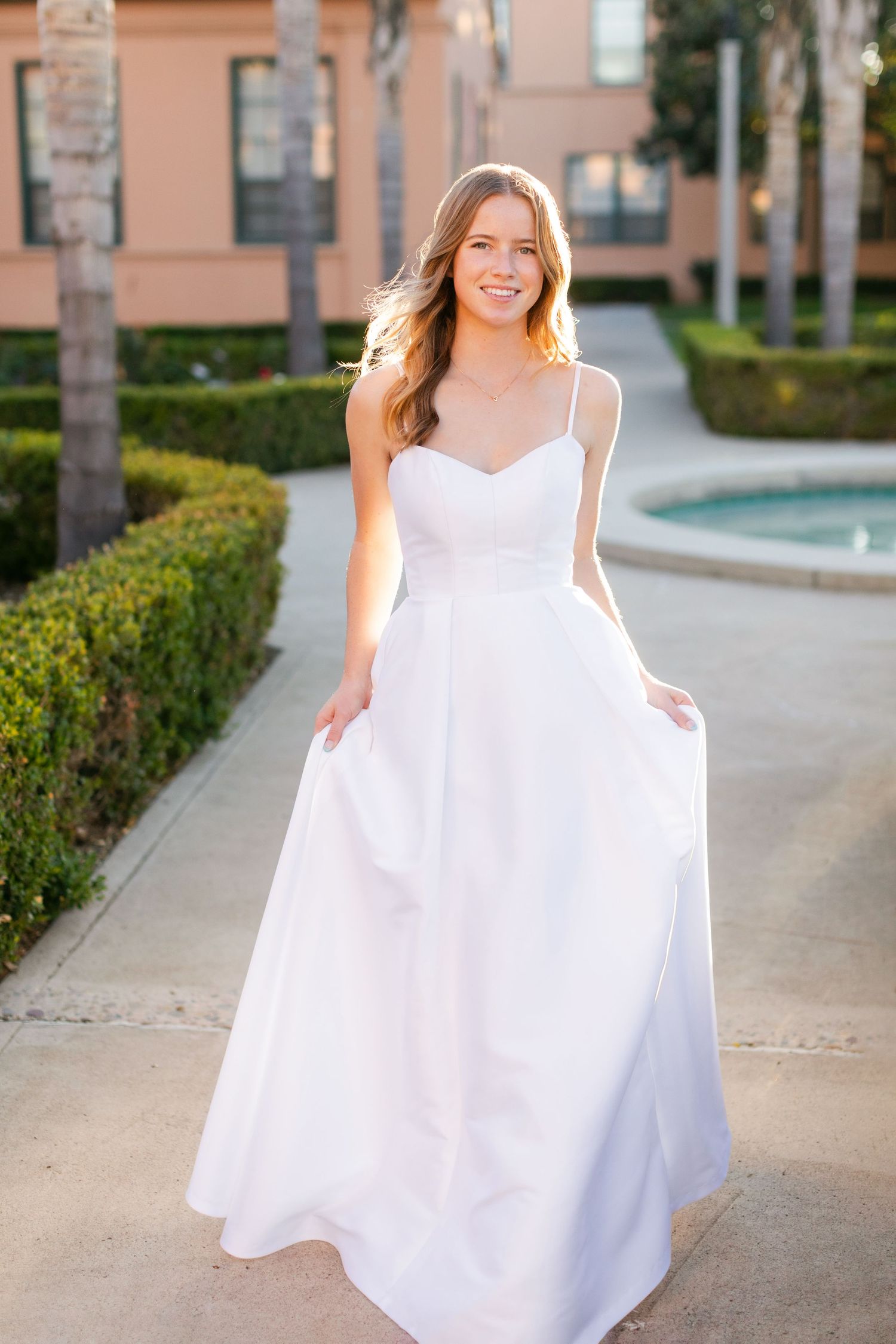 An elegant white wedding dress with spaghetti straps and a sweetheart neckline stands out against a garden path backdrop.