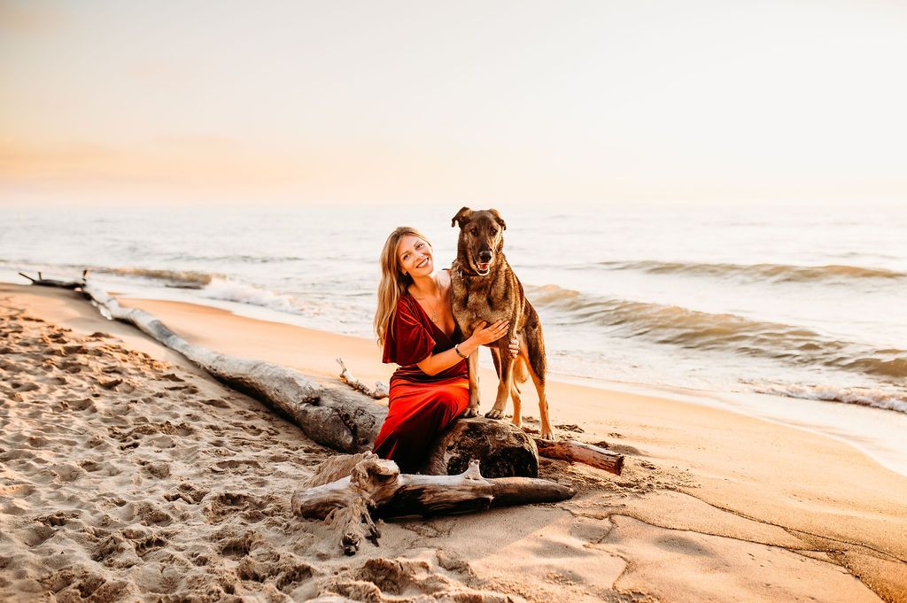A large dog poses with their companion on a scenic beach at sunset.