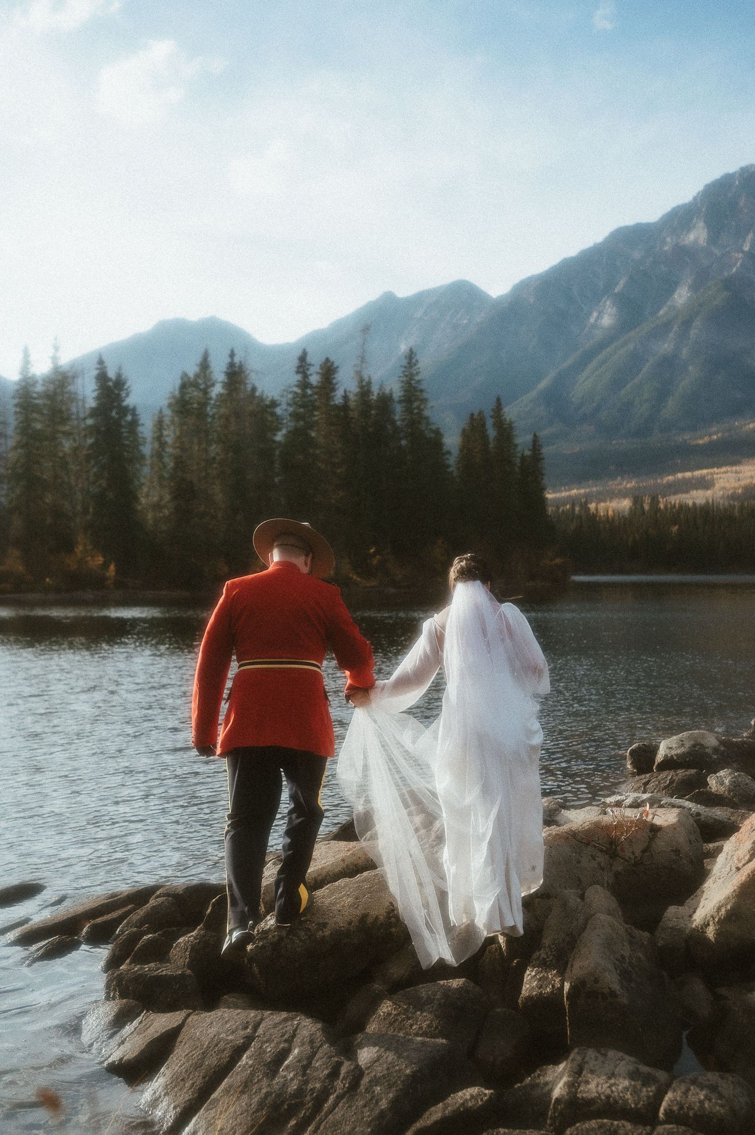 A couple in outdoor gear explores rocky lakeside terrain during their mountain wedding.