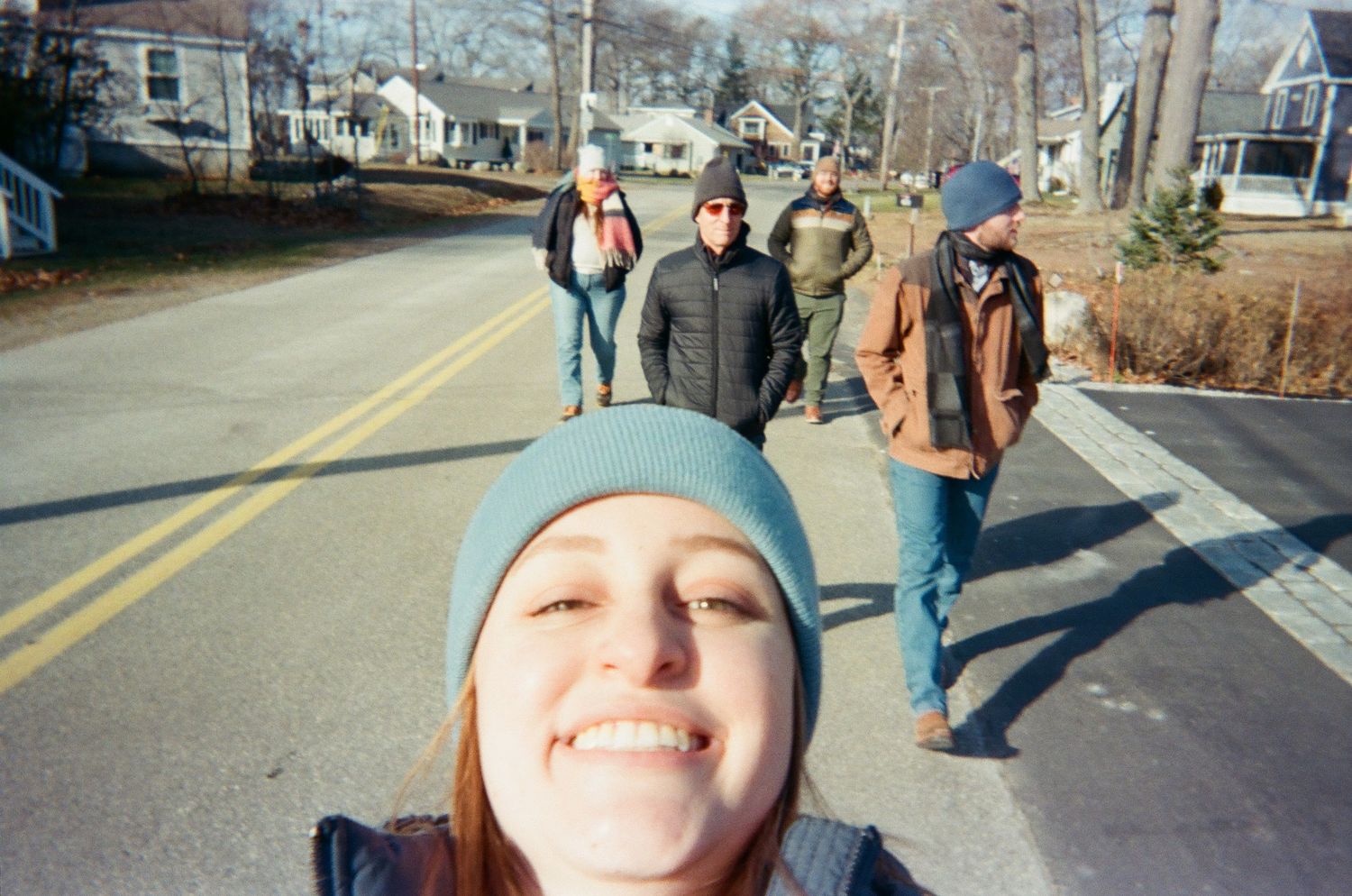 A smiling woman taking a group selfie while walking down a street with friends in Kennebunkport, Maine.