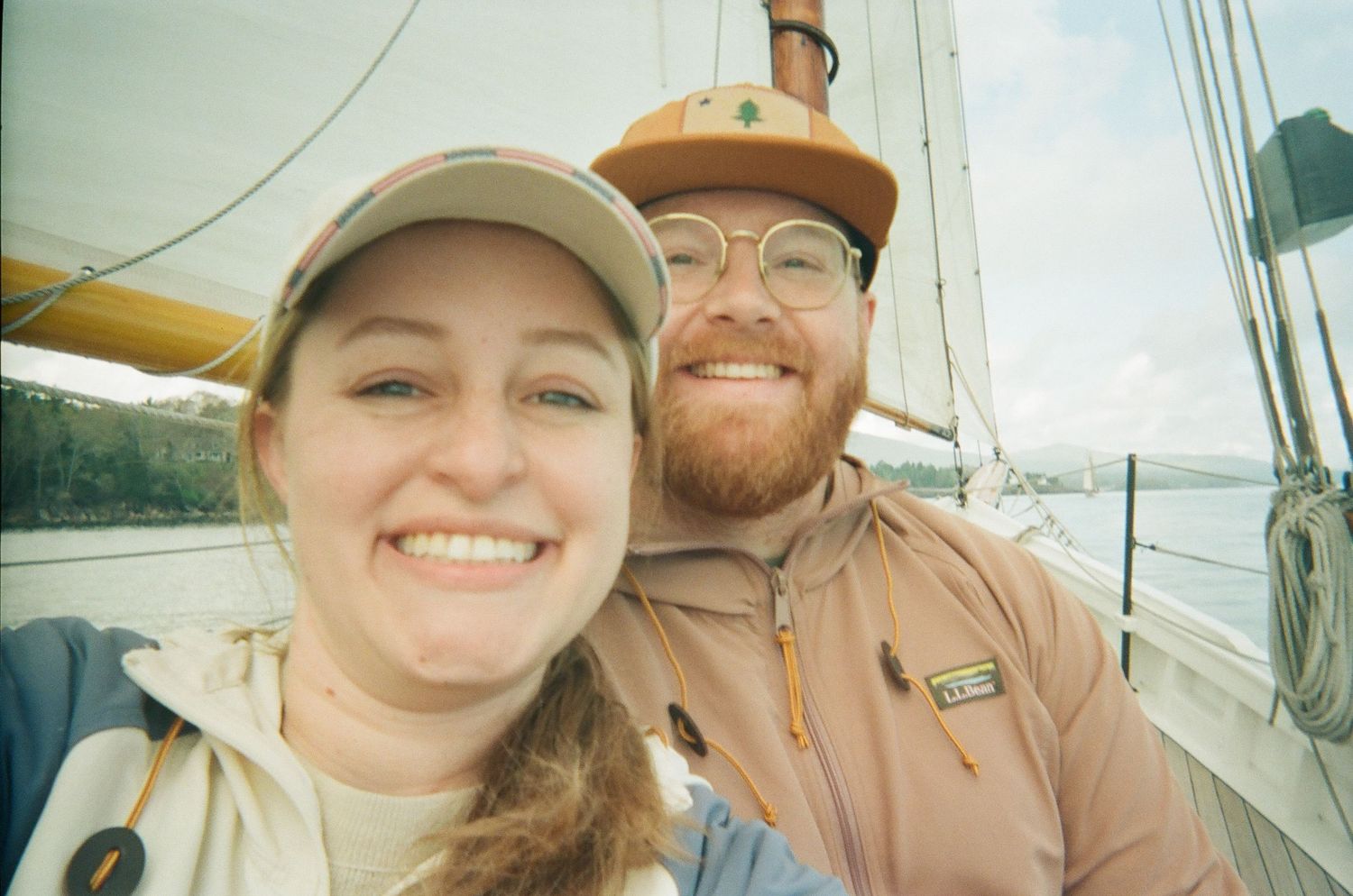 A smiling couple taking a selfie on a sailboat during a trip in Camden, Maine.