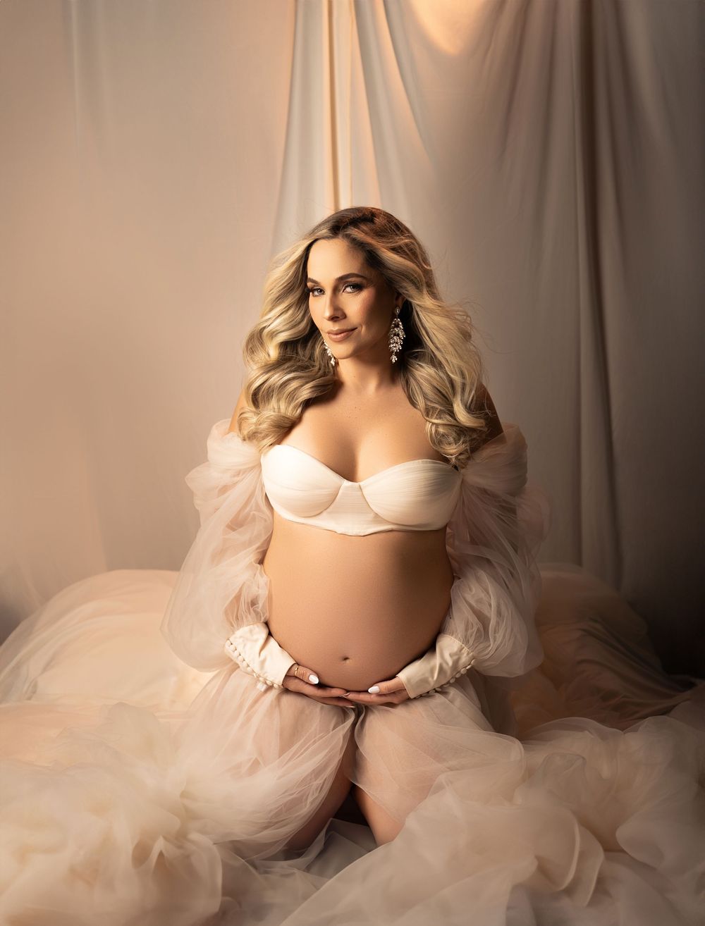 Artistic maternity portrait with flowing blush tulle fabric and soft lighting creating an ethereal, romantic mood.