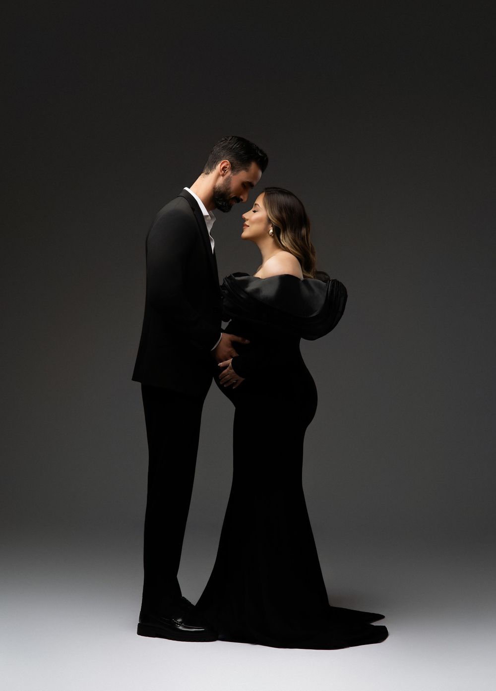 A couple in formal attire performs an elegant dance pose against a dark background with dramatic lighting.