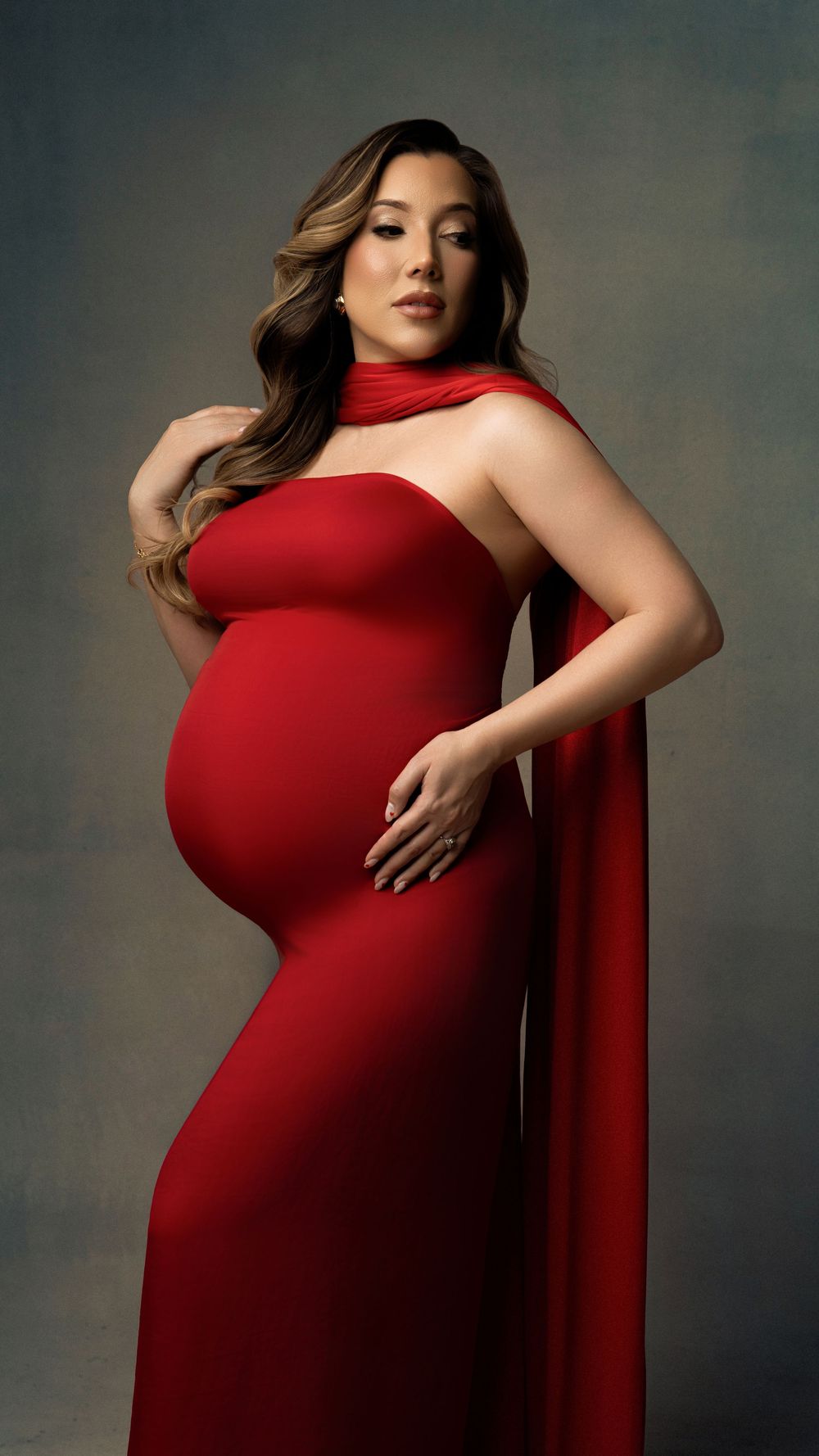 Artistic maternity photo series showing a woman in a flowing red dress against a dark studio backdrop.