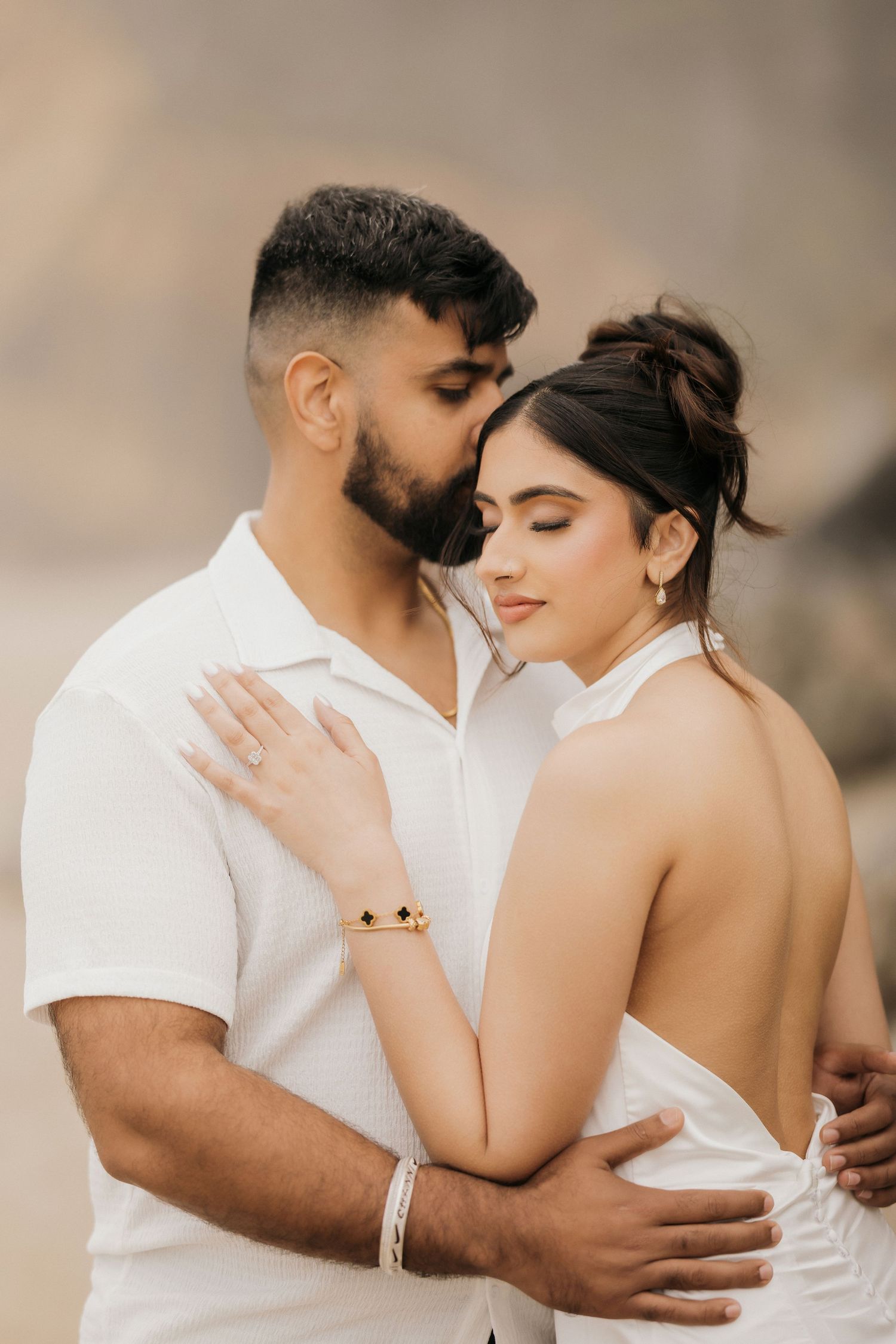 A couple in white outfits share an intimate moment against a neutral backdrop.