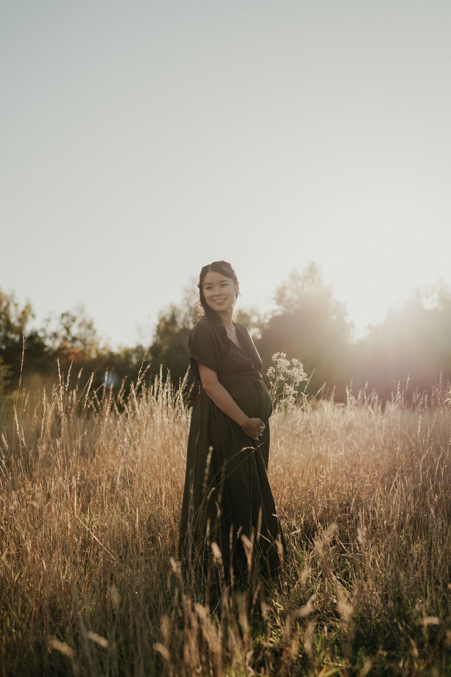 Ethereal maternity portrait in golden wildflower field at sunset.
