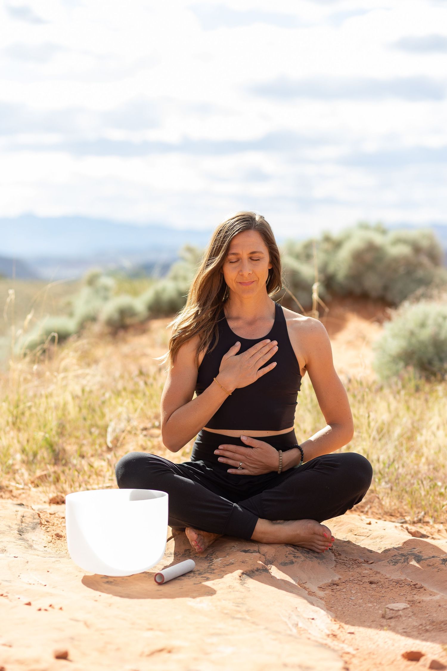 a woman meditating with hands on her heart in the desert with a sound bowl