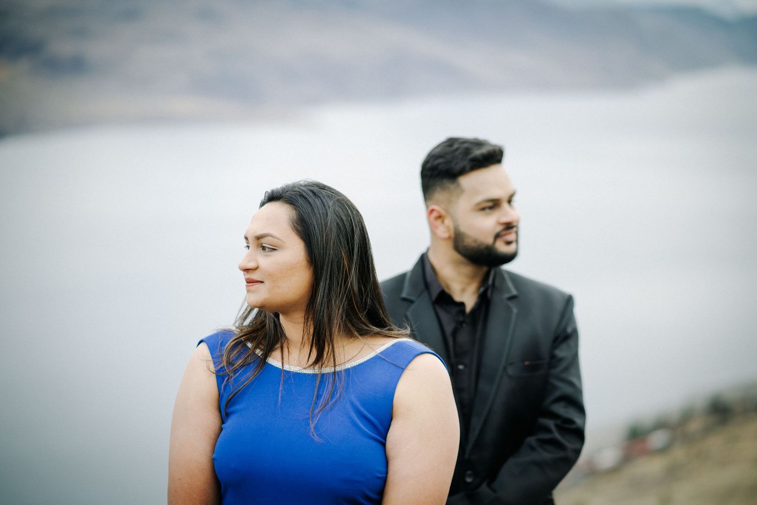 Couple in formal attire poses against misty mountain backdrop.