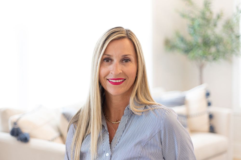 Professional headshot of a person in business attire against a bright home interior.