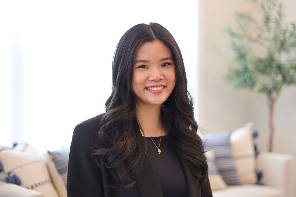 Professional headshot of a person in a dark blazer against a light interior background.