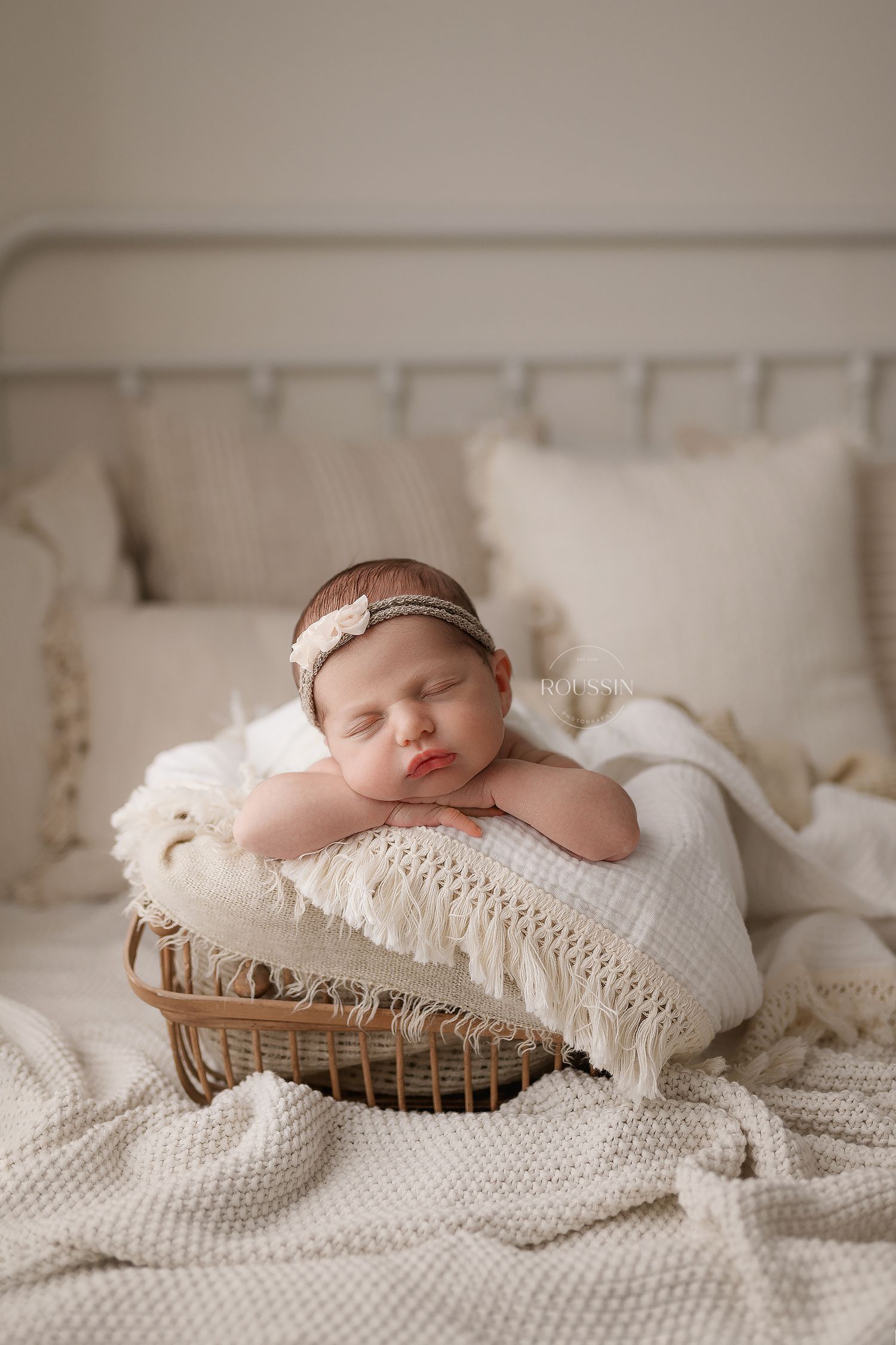 Sleeping newborn baby girl swaddled in white wrap wearing floral crown in a white wooden crib.