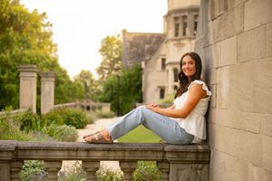 A person in casual attire relaxes on a stone ledge outdoors during golden hour lighting.
