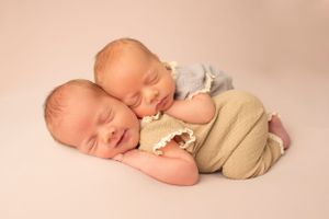 Peaceful portrait of sleeping newborn twins cuddling on soft beige backdrop.