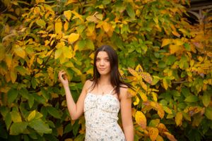 Summer portrait in white dress against backdrop of yellow and green leaves.