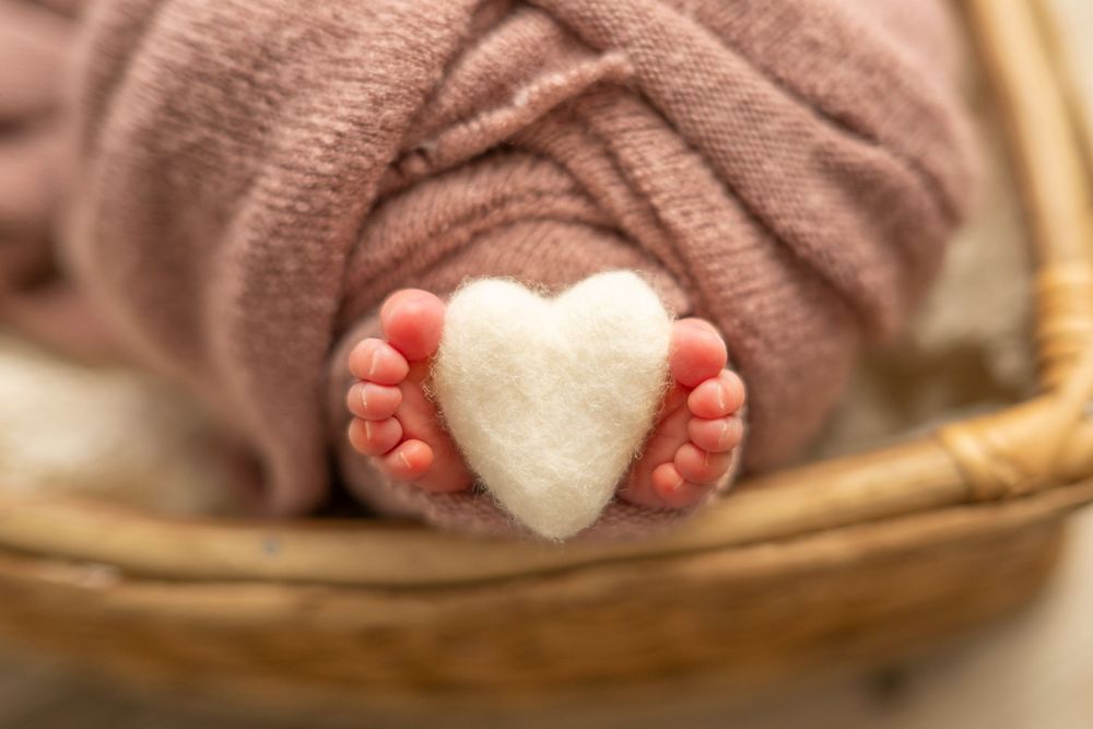 Hands hold and shape a small heart made from white rice against a wooden background.