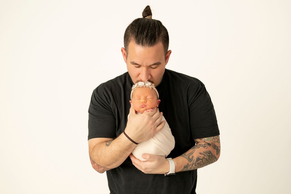 Man in black shirt with tattoos holds and kisses white ceramic mug in artistic portrait series.