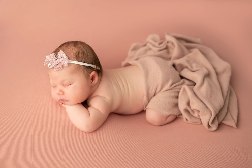 Newborn baby sleeping peacefully on soft pink background with gentle lighting and delicate fabric textures.