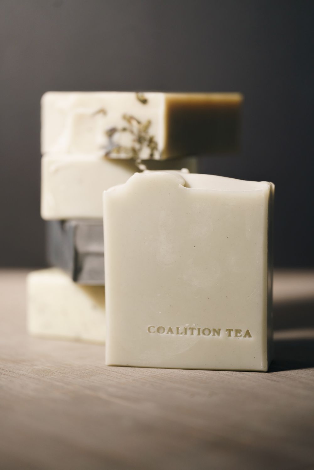 Coalition Tea branded artisan soap bars stacked on a wooden surface, showcasing natural handcrafted soaps in cream and dark tones.
