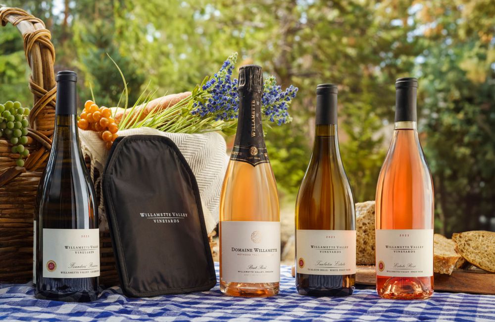 Various wine bottles including rosé and white varietals arranged outdoors with a woven basket and gray bag in natural lighting.