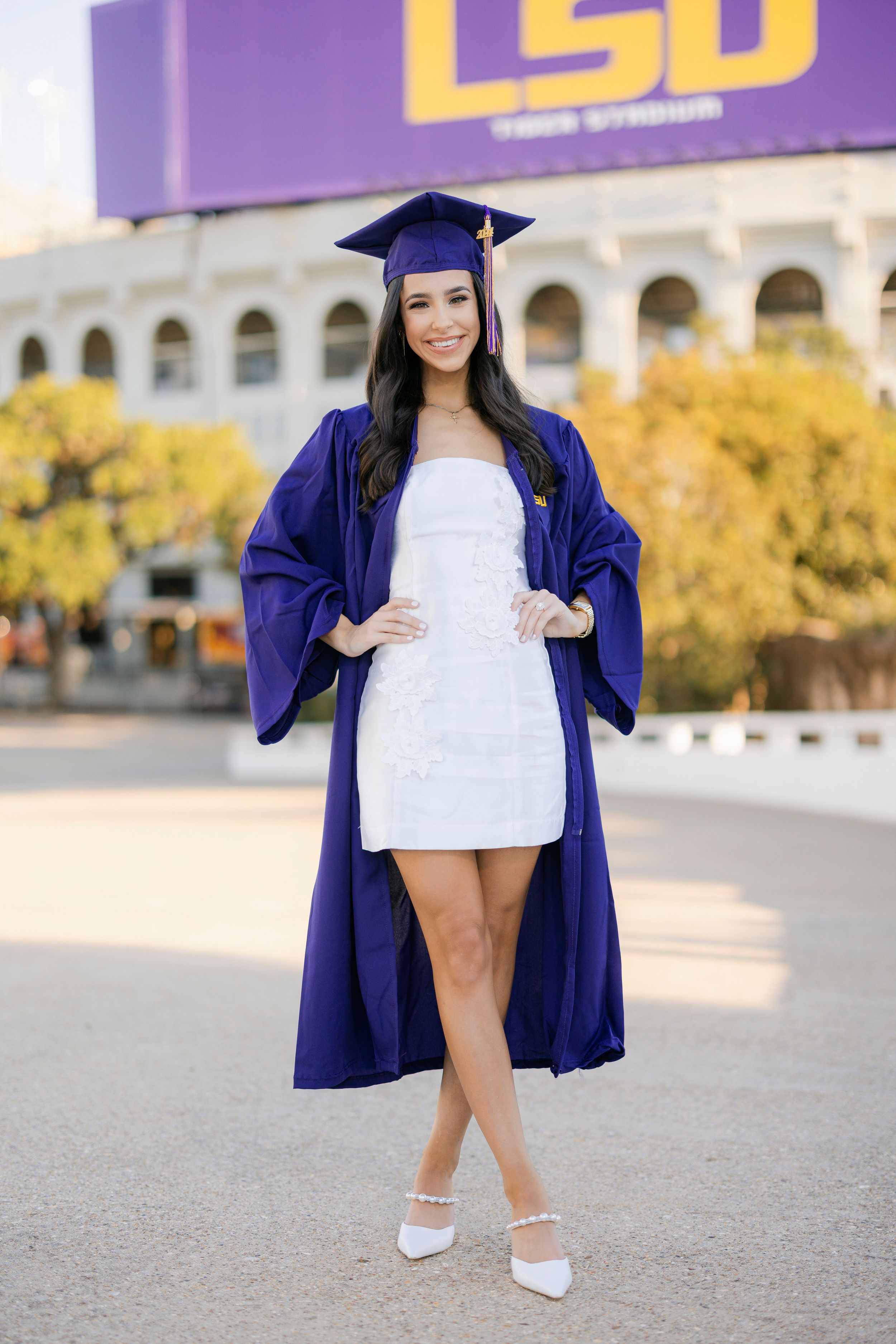 College graduate in blue cap and gown holding diploma on LSU campus during graduation photo session.