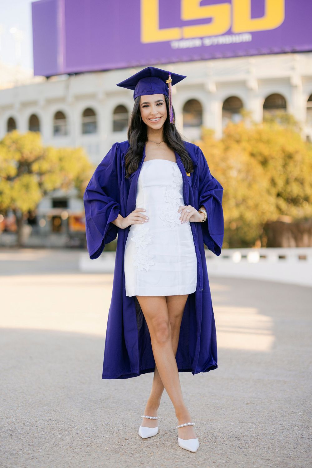 College graduate in blue cap and gown holding diploma on LSU campus during graduation photo session.