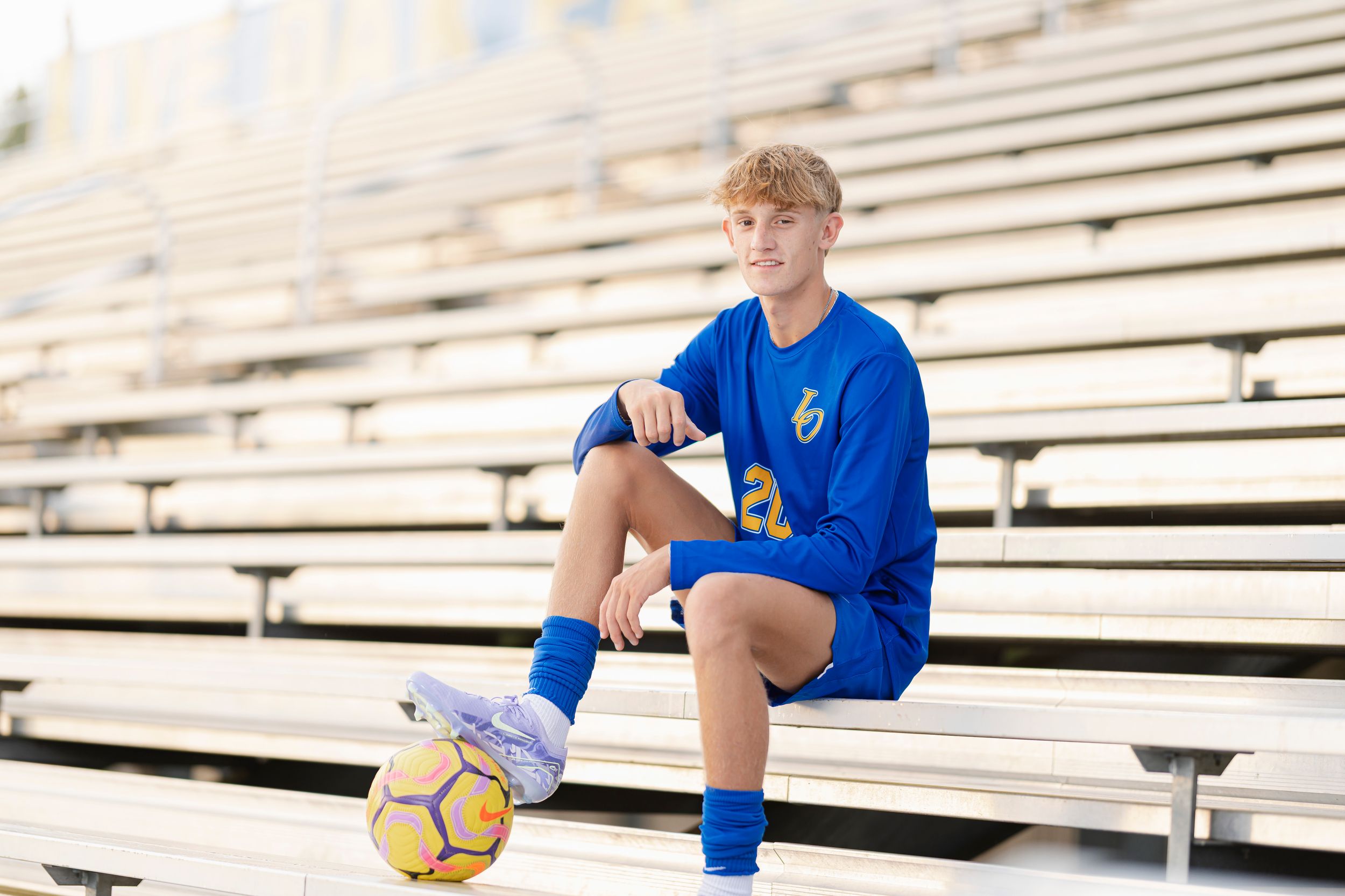 Soccer players in blue jerseys train together on bleachers with a ball during outdoor practice session.