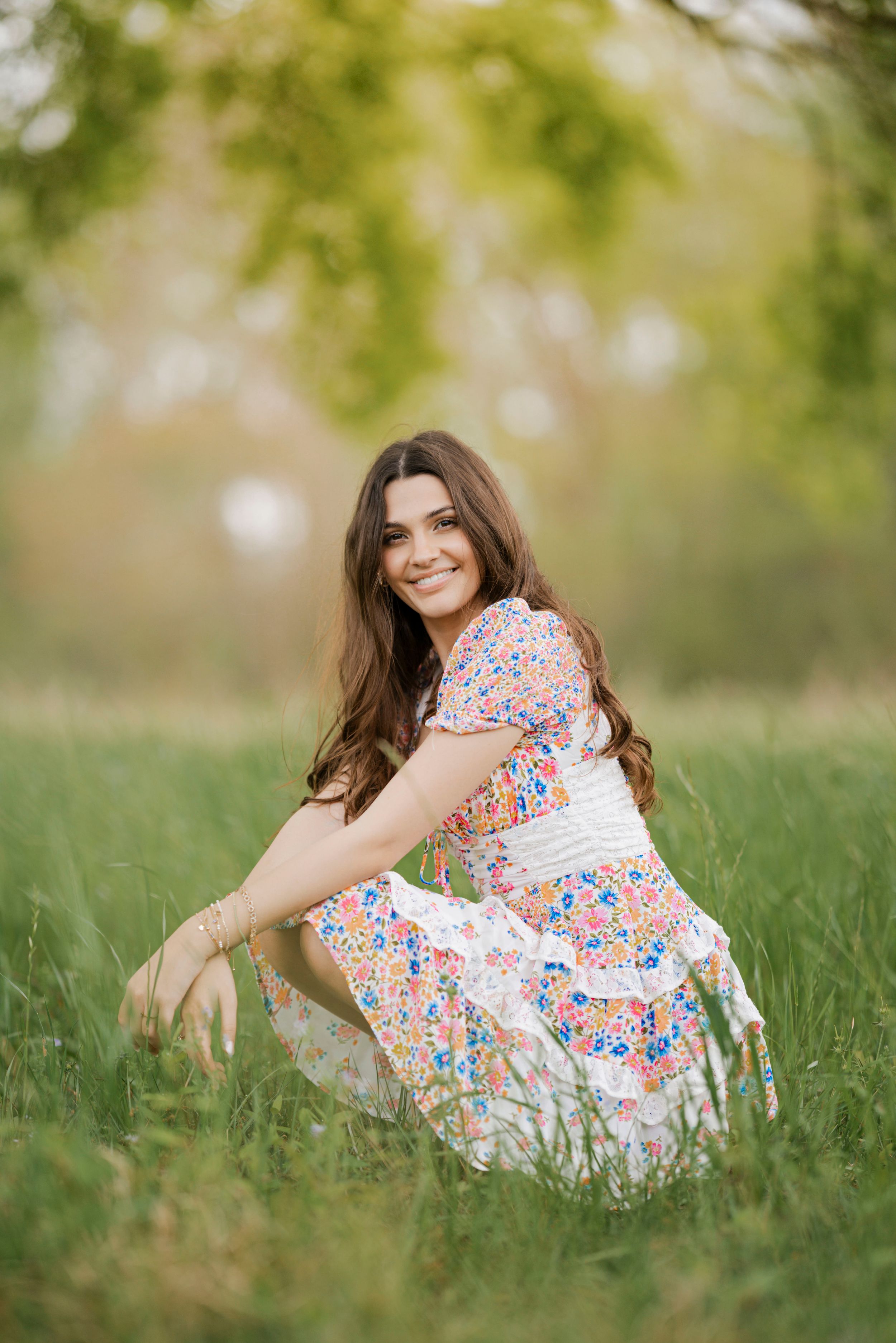 A person in a floral print dress lies on green grass in a dreamy outdoor setting during a photo session.