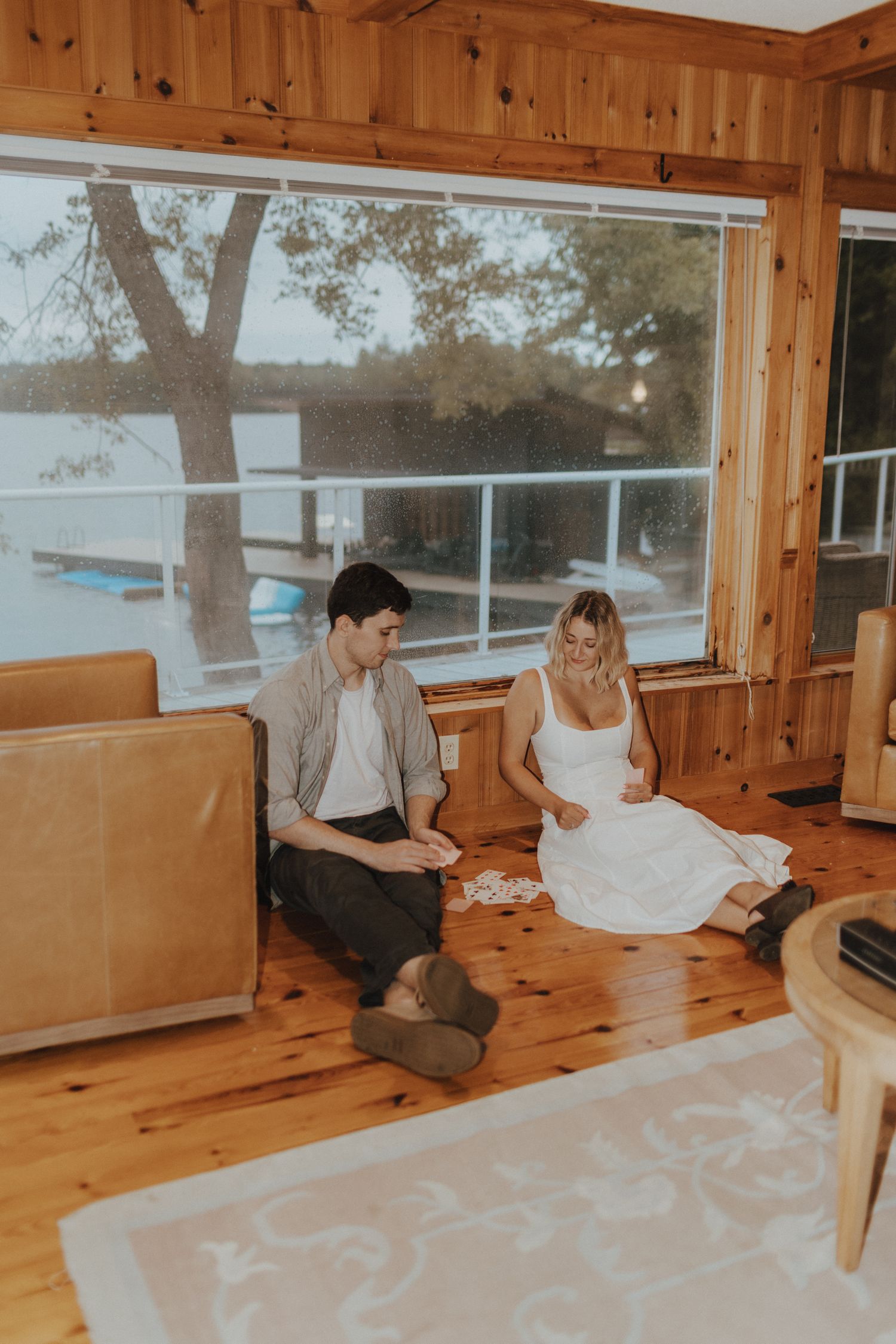 Couple sitting on wooden benches in a rustic cabin with large windows.